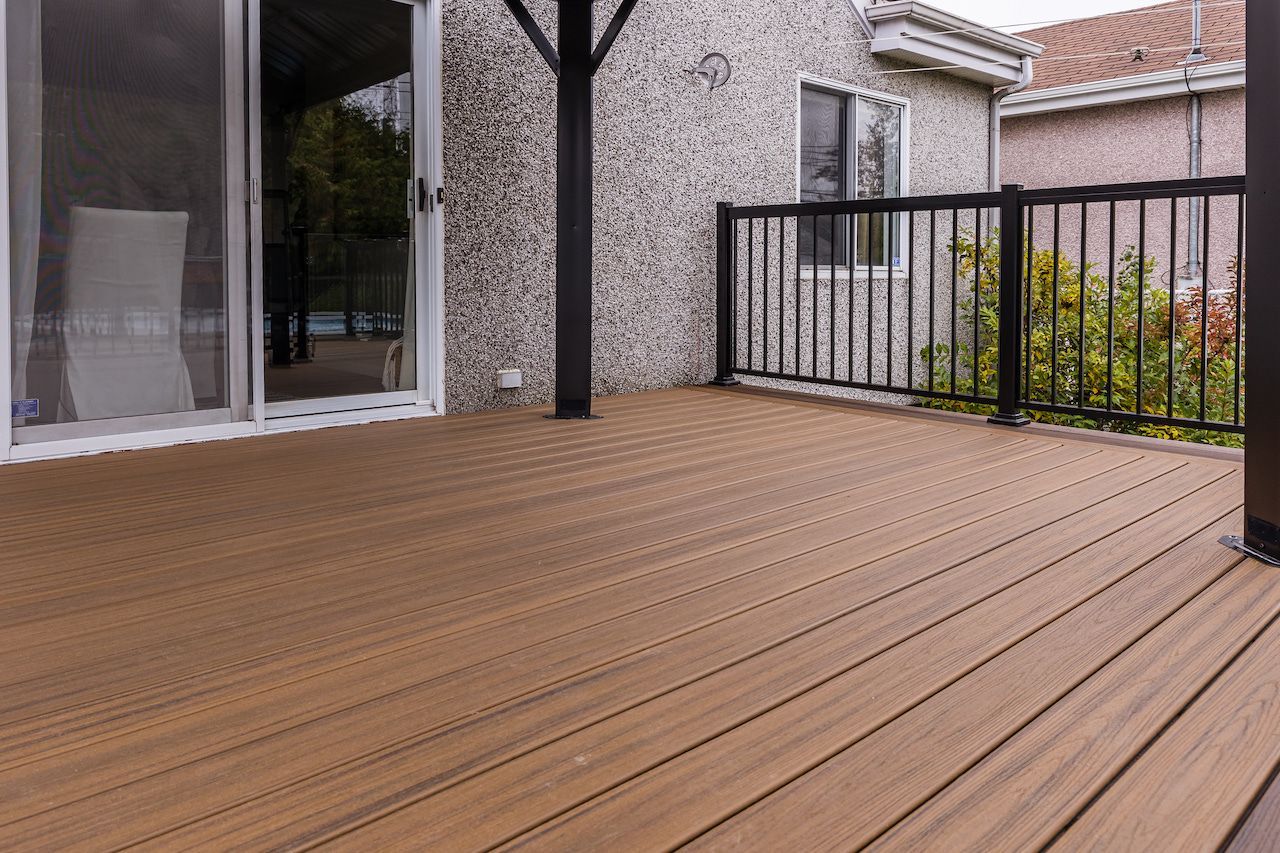 Terrasse en composite marron avec rambarde et poteaux porteurs noirs, jouxtant une maison avec une porte-fenêtre coulissante.