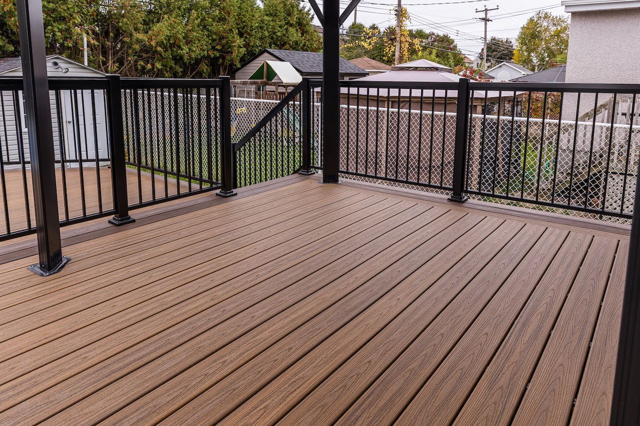 Terrasse en composite marron avec rambarde en métal noir, sous un gazebo.