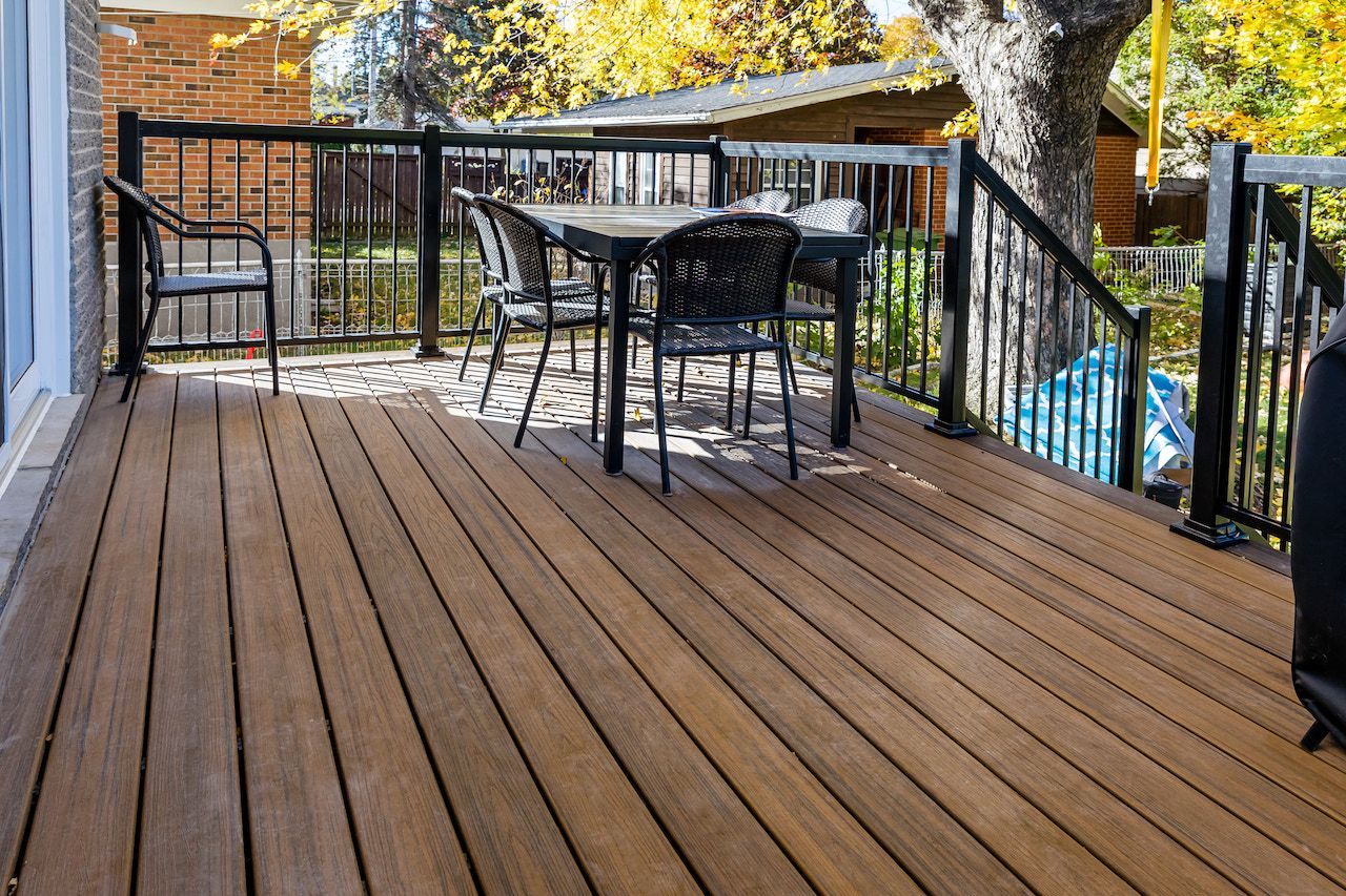 Terrasse en bois avec rambarde noire, table et chaises. Feuillage d'automne en arrière-plan.