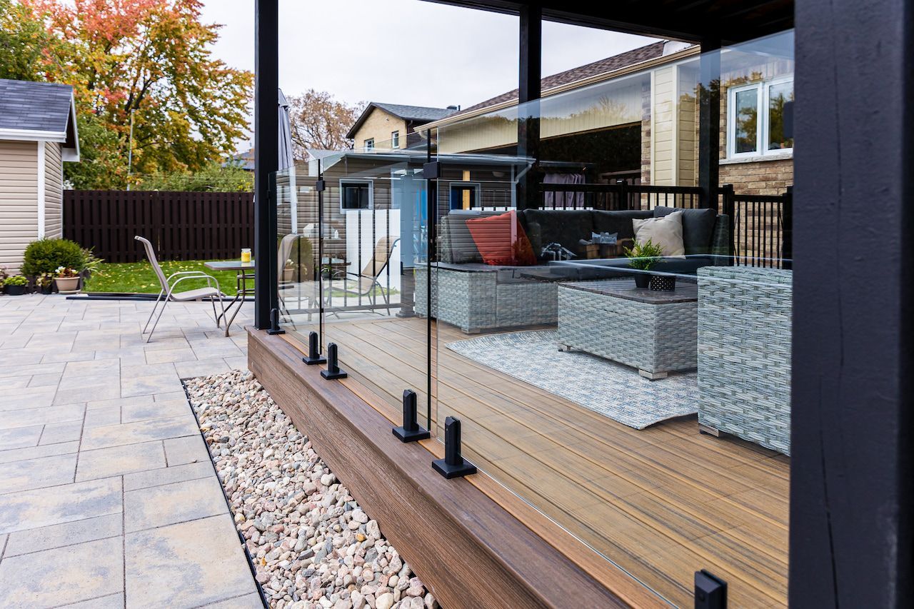 Patio vitré avec mobilier en osier. Terrasse en bois, dalles et aménagement paysager.