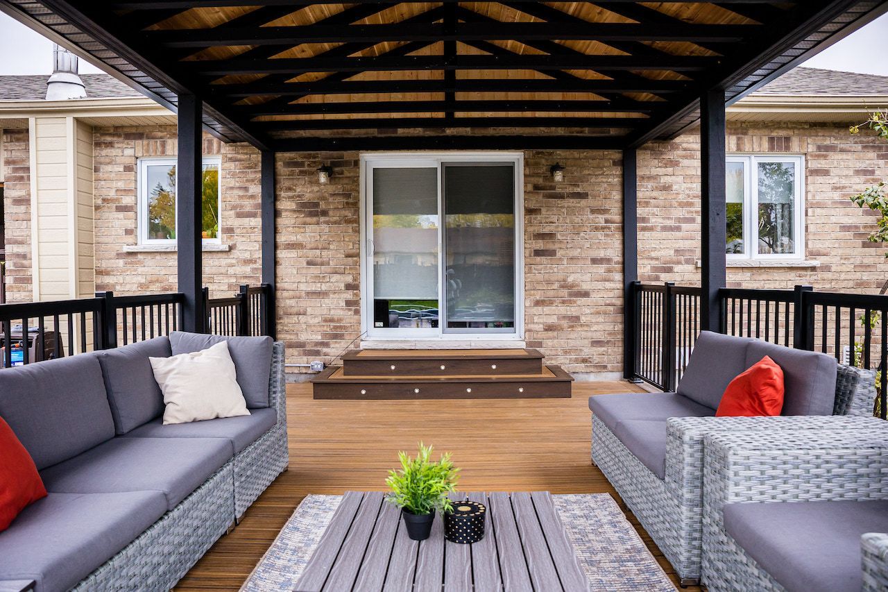 Terrasse extérieure avec canapés gris, terrasse en bois et structure sombre au-dessus.