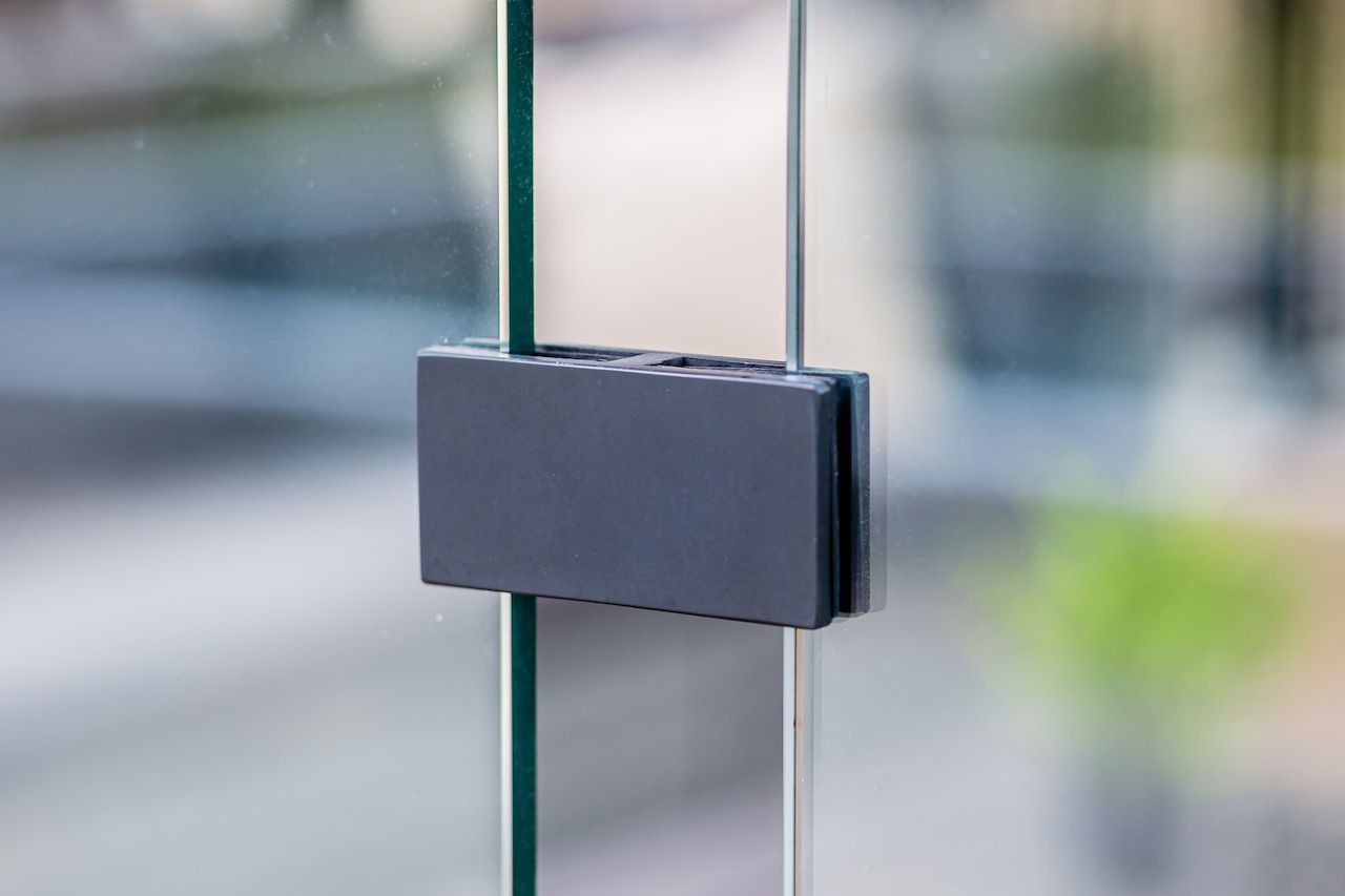 Charnière de porte rectangulaire noire fixant deux panneaux de verre.