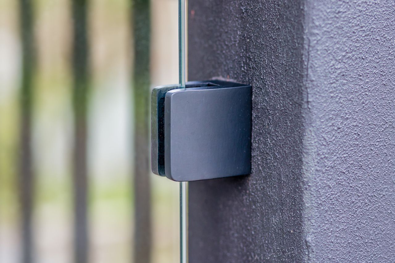 Support gris foncé maintenant un panneau de verre contre un mur sombre texturé.
