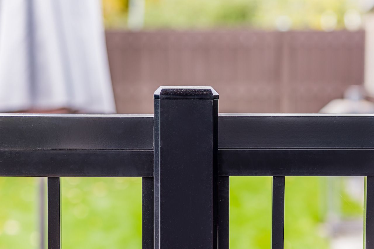 Poteau et barreaux de rambarde en métal noir sur fond de jardin vert flou.