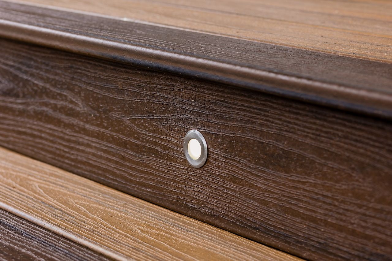 Gros plan sur des marches de terrasse en composite avec un luminaire encastré. Finition grain de bois brun foncé.