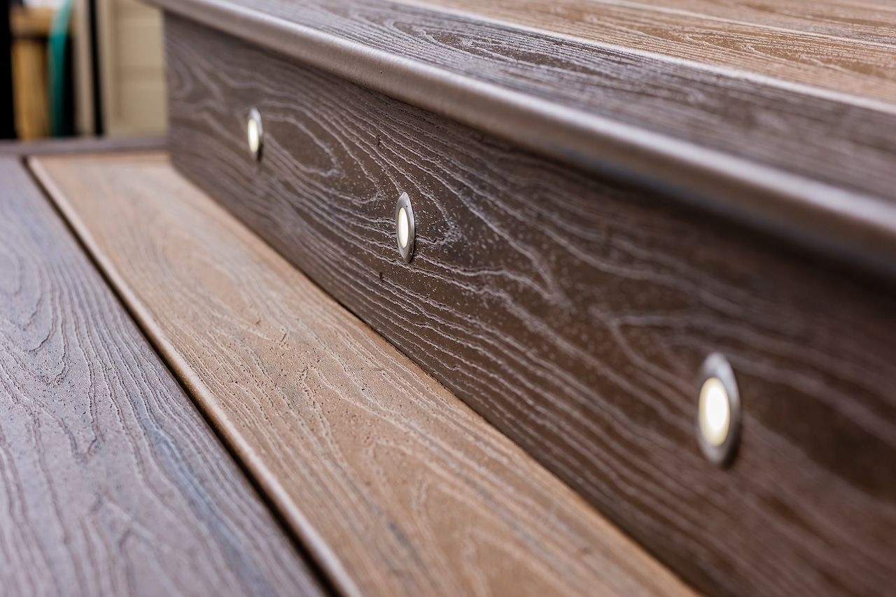Gros plan sur les marches composites d'une terrasse avec éclairage intégré ; tons de bois clair et brun.