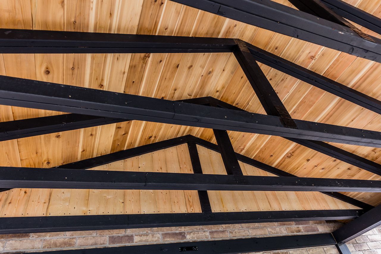 Plafond en bois avec poutres métalliques noires dans un cadre extérieur.