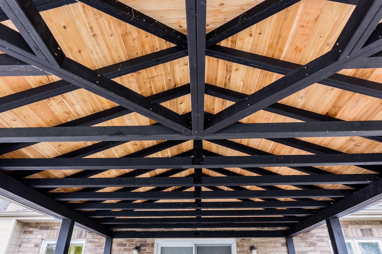 Plafond en pergola de bois noir avec poutres diagonales au-dessus de panneaux de bois naturel.