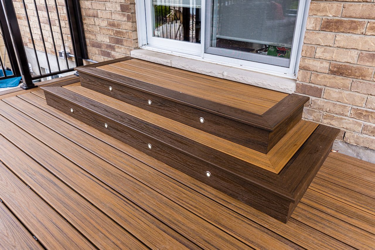 Terrasse composite avec deux marches et éclairage intégré, menant à une porte coulissante en verre.