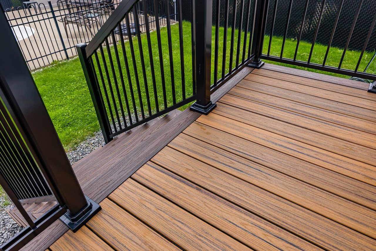 Terrasse en bois avec balustrade noire donnant sur une cour gazonnée.