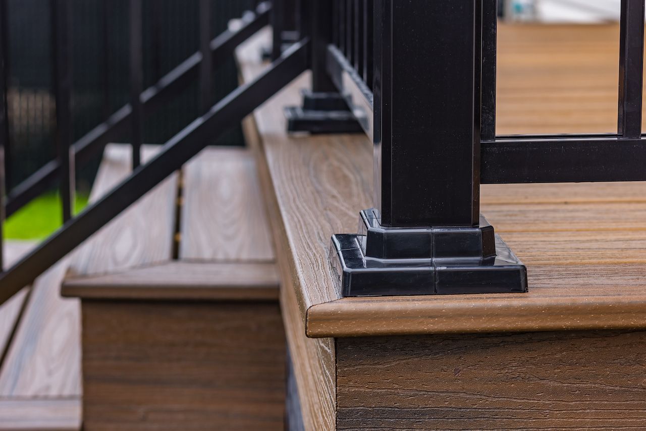Gros plan sur un escalier de terrasse en composite avec poteaux et mains courantes noirs.