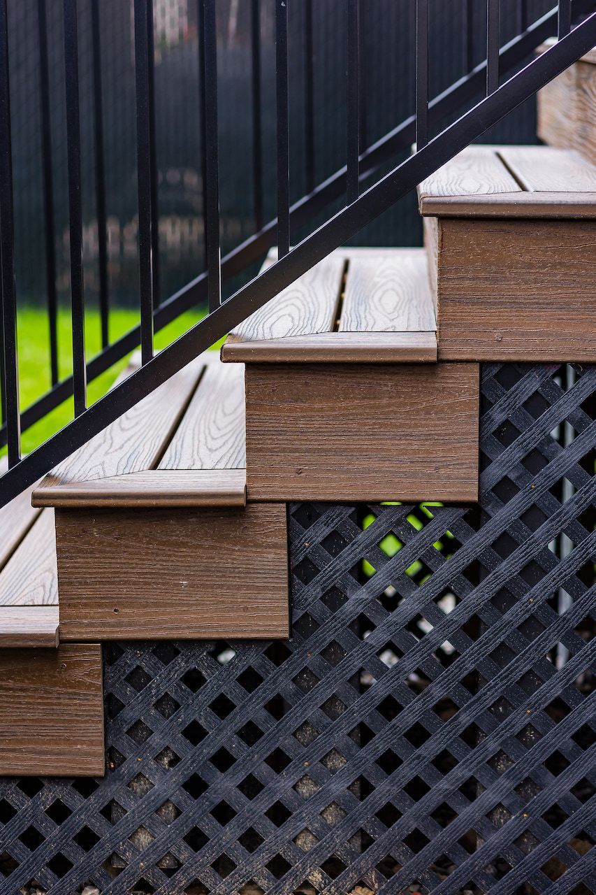 Escalier de terrasse marron avec rambarde et treillis noirs, installé à l'extérieur.