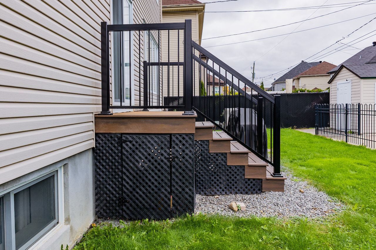 Escalier extérieur avec rampe noire, marches en composite et plinthe décorative en treillis.