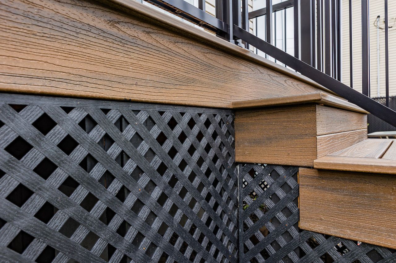 Terrasse composite avec plinthe et rambarde en treillis. Terrasse et escalier bruns. Treillis gris foncé.
