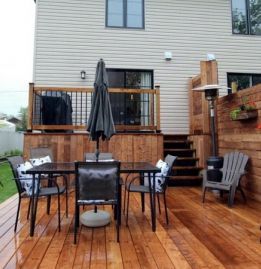 Terrasse arrière avec table et chaises, parasol, chauffage et escalier menant à la maison.