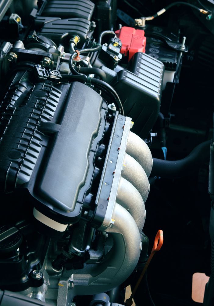 Car engine bay with black covers, silver exhaust manifold, and orange oil dipstick.