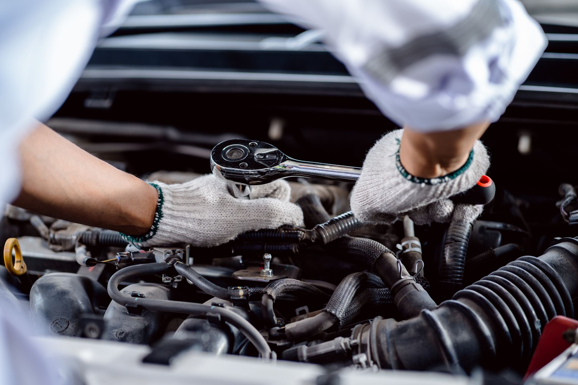 Mechanic in gloves using a wrench on a car engine.