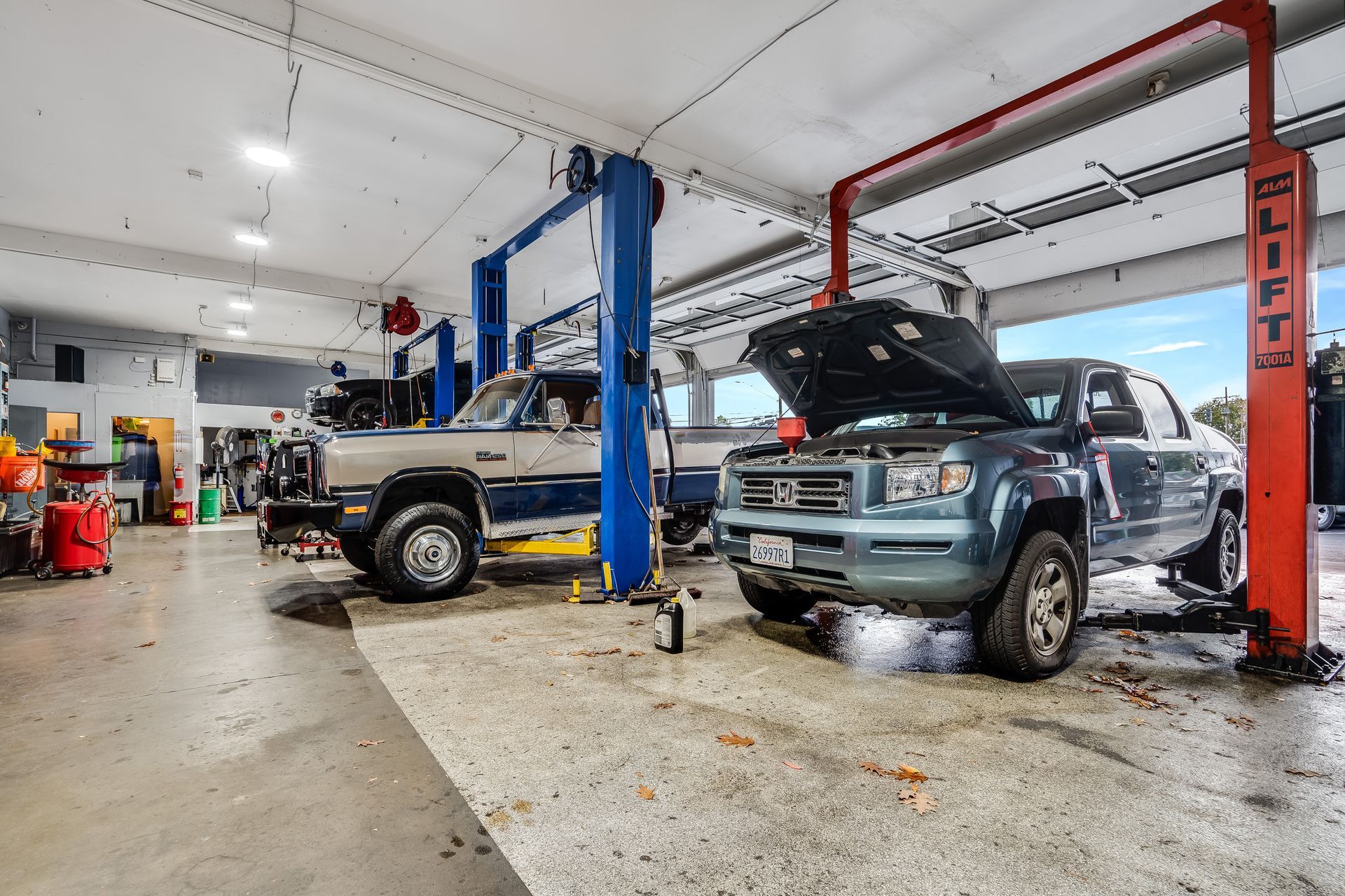 Two trucks on lifts in a brightly lit auto repair shop; one has an open hood.