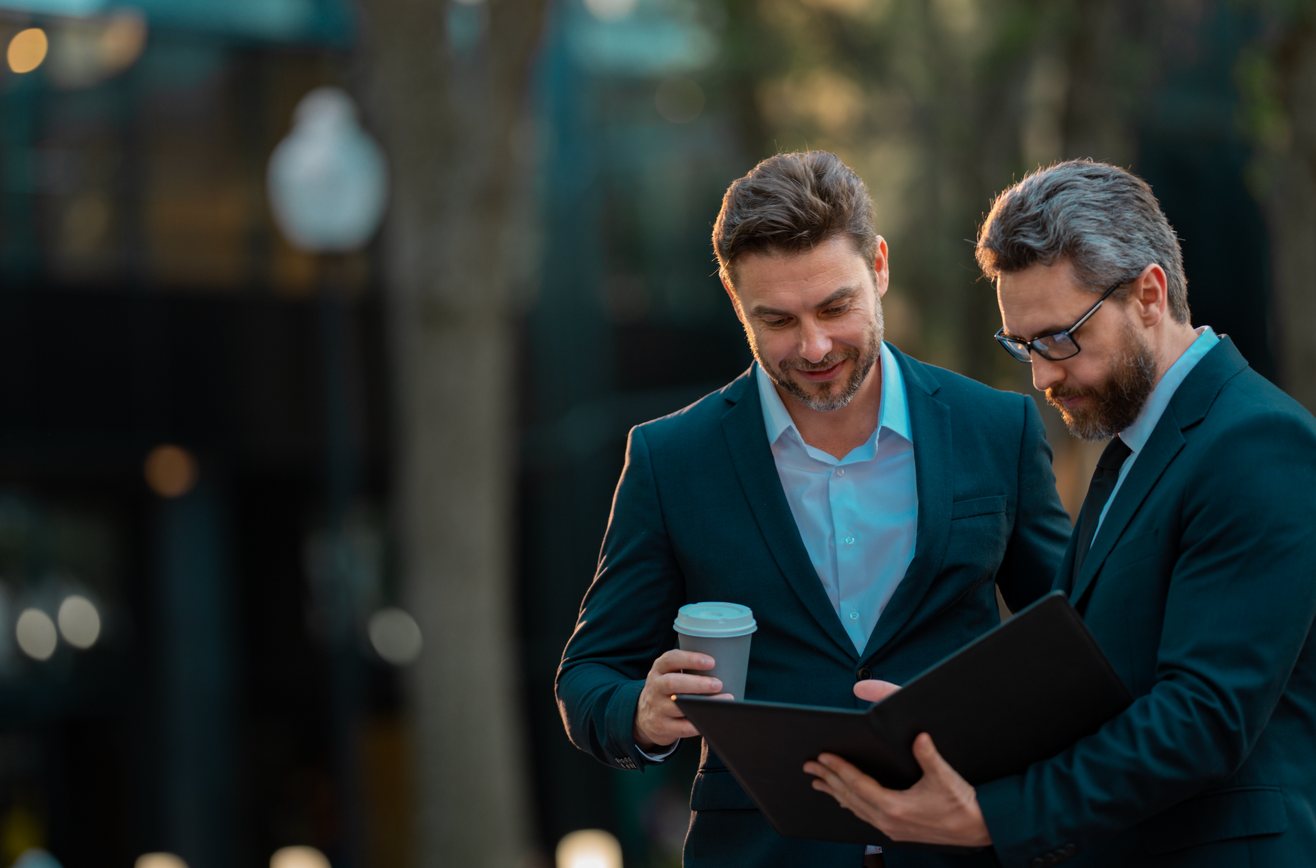 Two men in suits are looking at a clipboard.