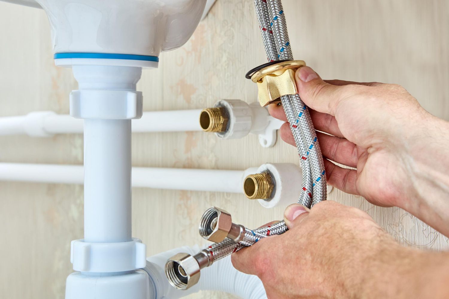 Hands connecting braided water supply hose to a bathroom sink drain and faucet plumbing under the sink
