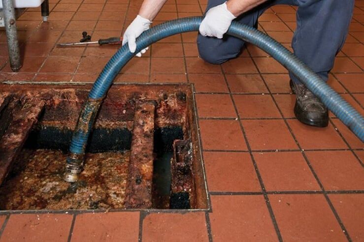 Worker using a hose to clean a rusted floor drain in a tiled floor