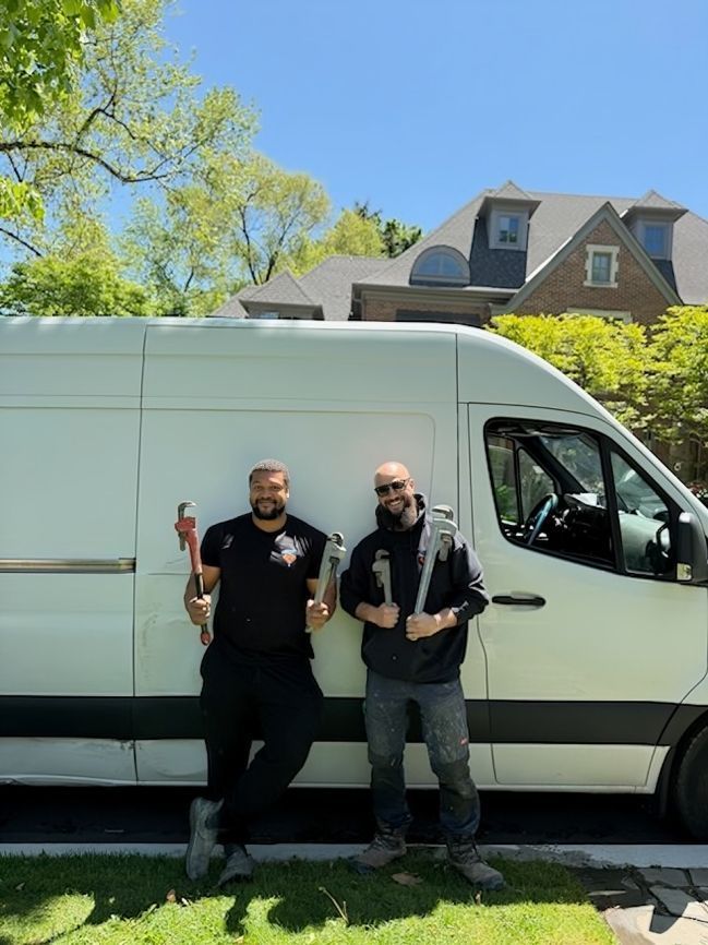 Two people standing beside a white van on a sunny street, smiling and holding drinks.