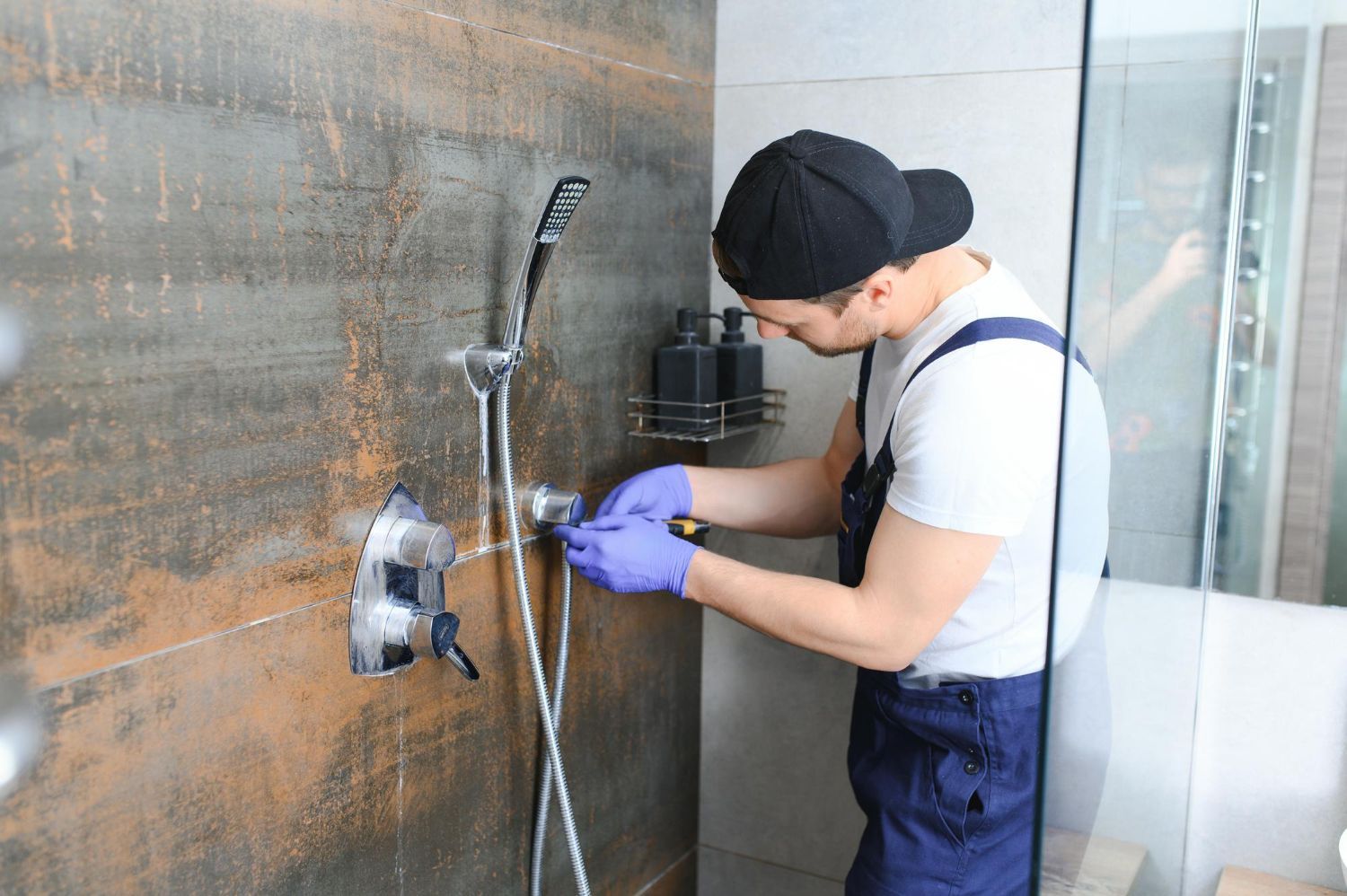 Technician in purple gloves adjusting a wall-mounted shower fixture in a tiled bathroom