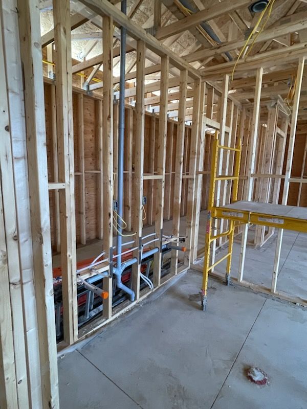 Interior of a house under construction with exposed wooden framing, concrete floor, and tools visible.