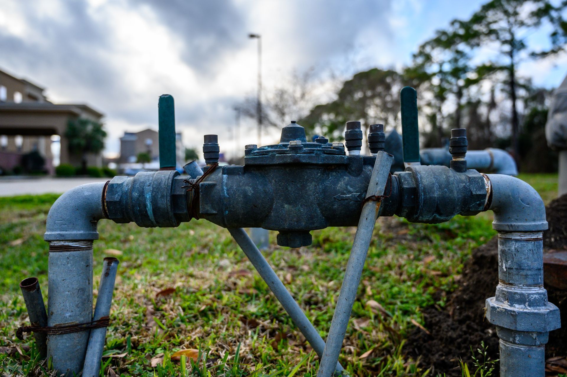 Rusty outdoor pipeline assembly on grass with a blurred house in the background
