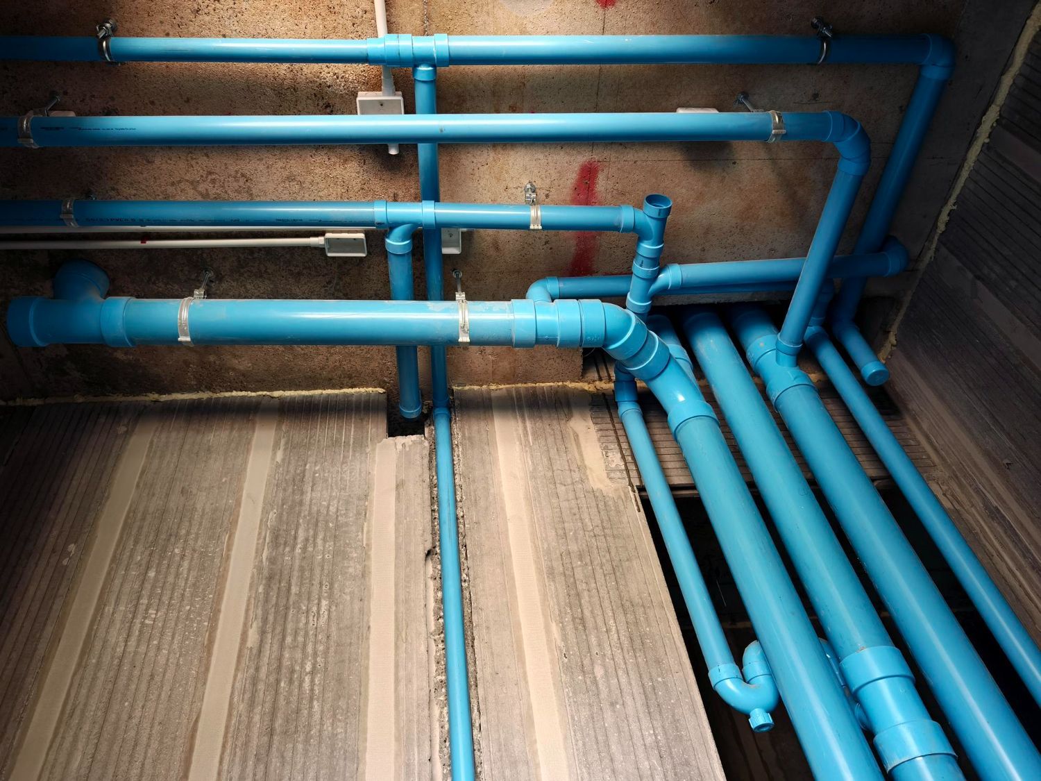 Blue utility pipes running along a wall and floor in a basement or industrial room.
