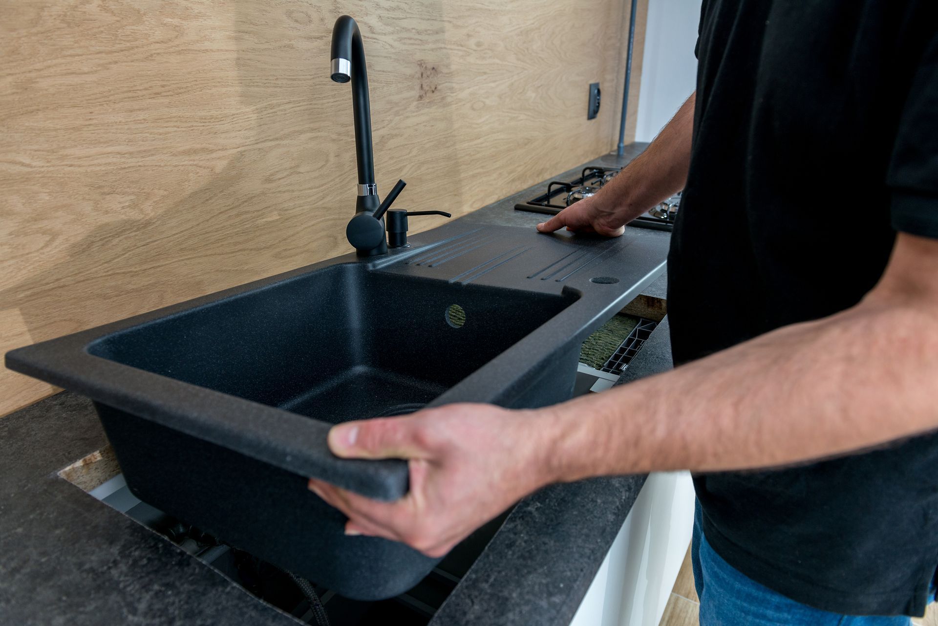 A man is holding a black sink in his hands in a kitchen.