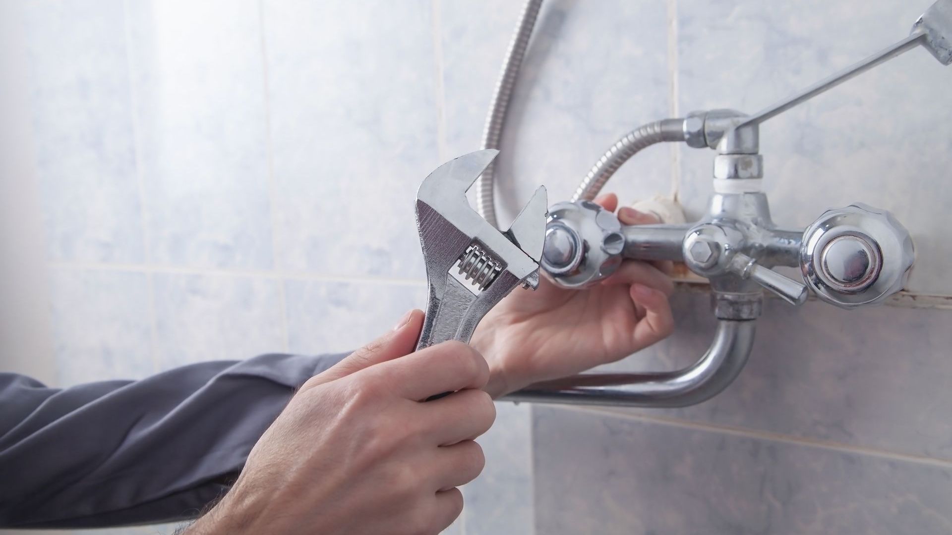 A person is fixing a shower head with a wrench.