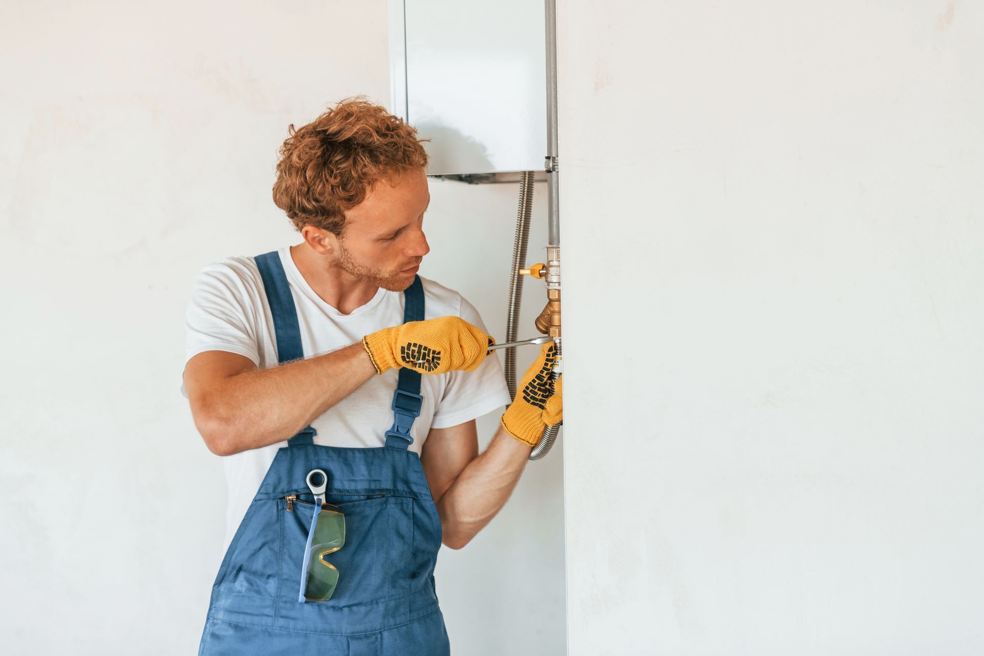 A man in overalls is fixing a heater on a wall.