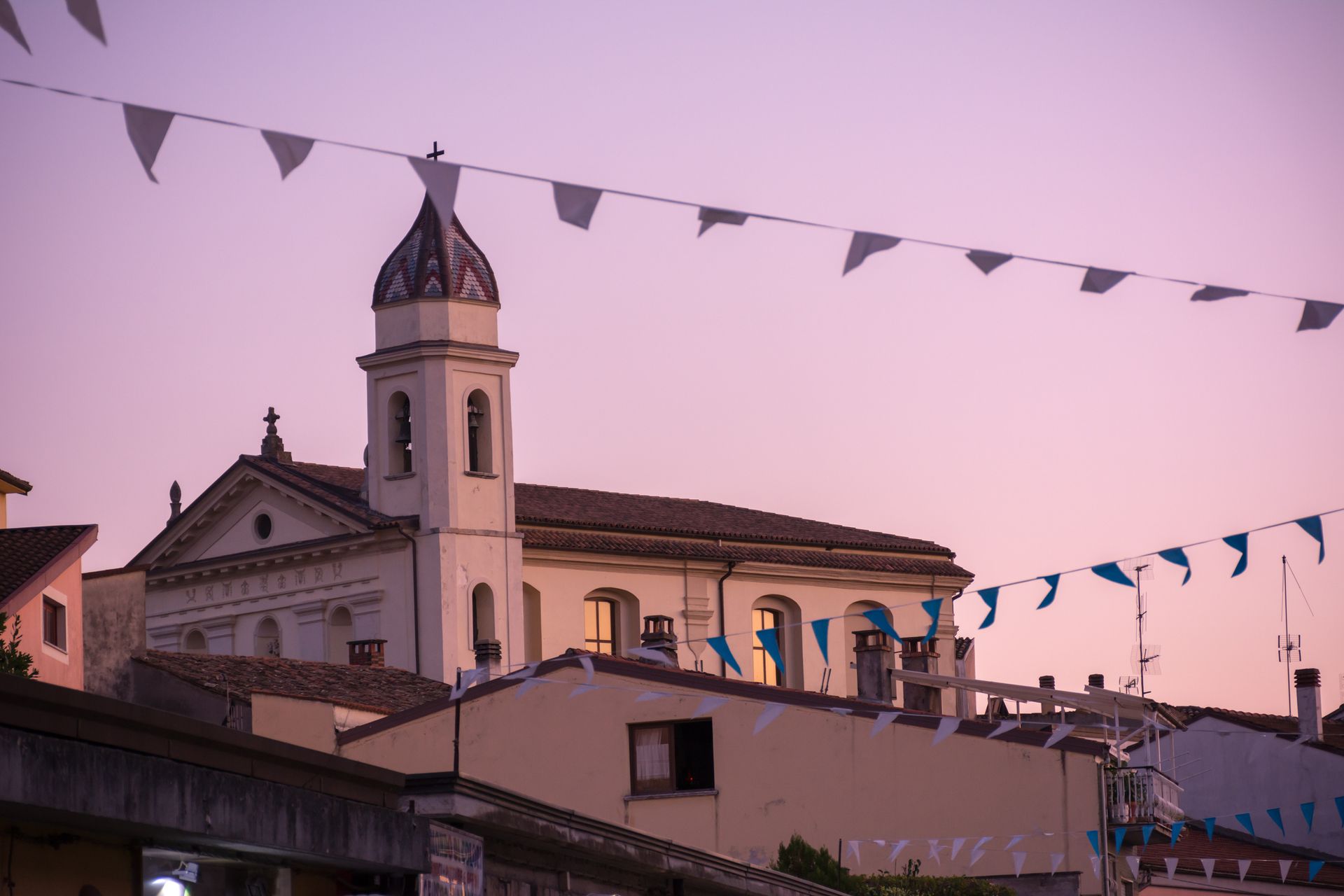 Campanile e tetti della chiesa al crepuscolo, con un cielo viola e bandierine che sventolano sopra la testa.