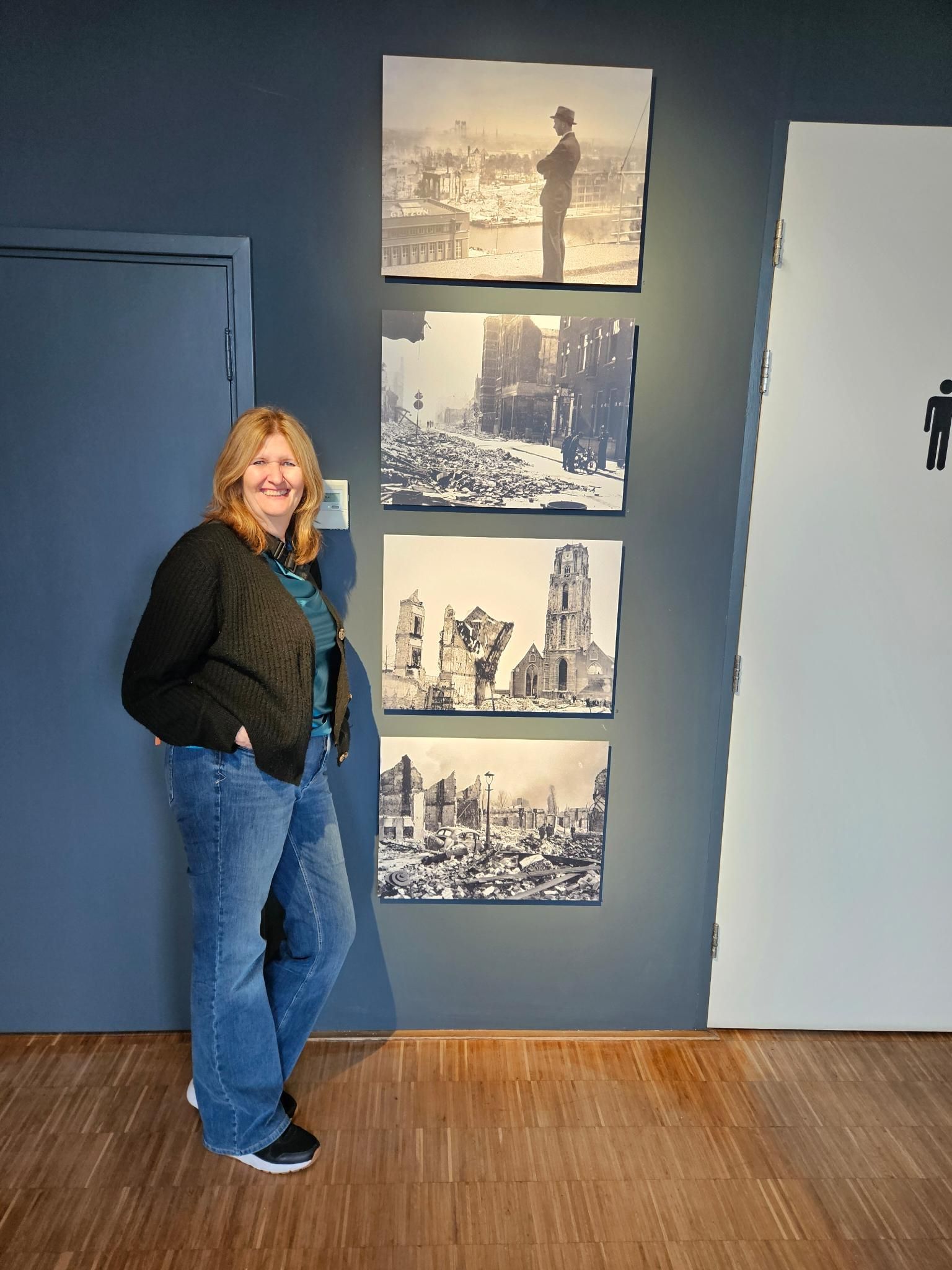 Een vrouw staat naast vier ingelijste, historische zwart-witfoto's aan een blauwe muur.