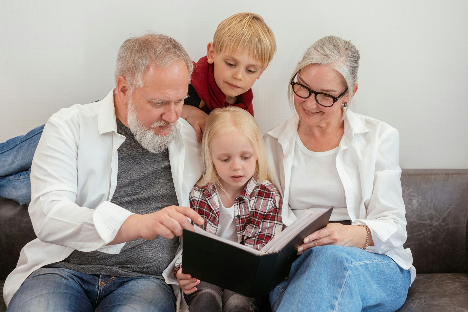 Two adults and two children sit on a sofa, looking together at an open photo album held by one of the children.