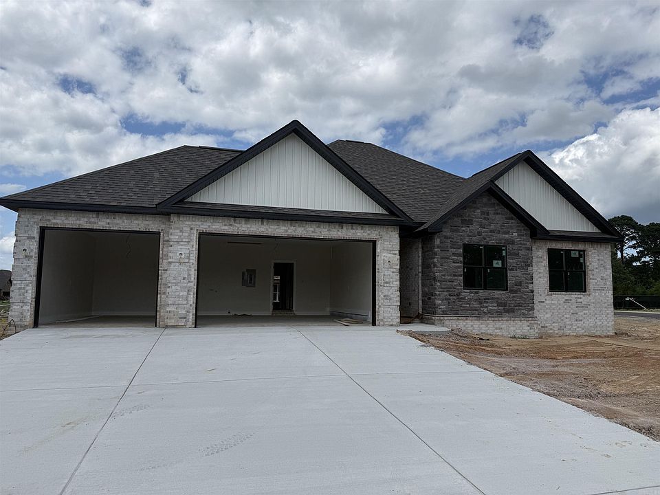 New single-story house with stone facade, three-car garage, and large concrete driveway under cloudy sky