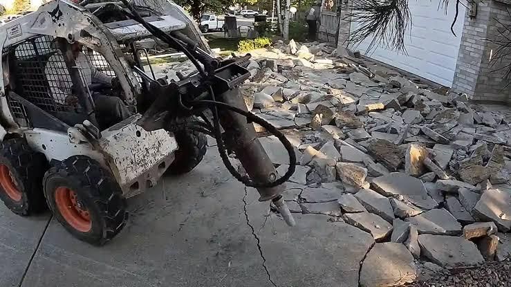 A skid steer loads rubble from a collapsed stone wall beside a building and pool.