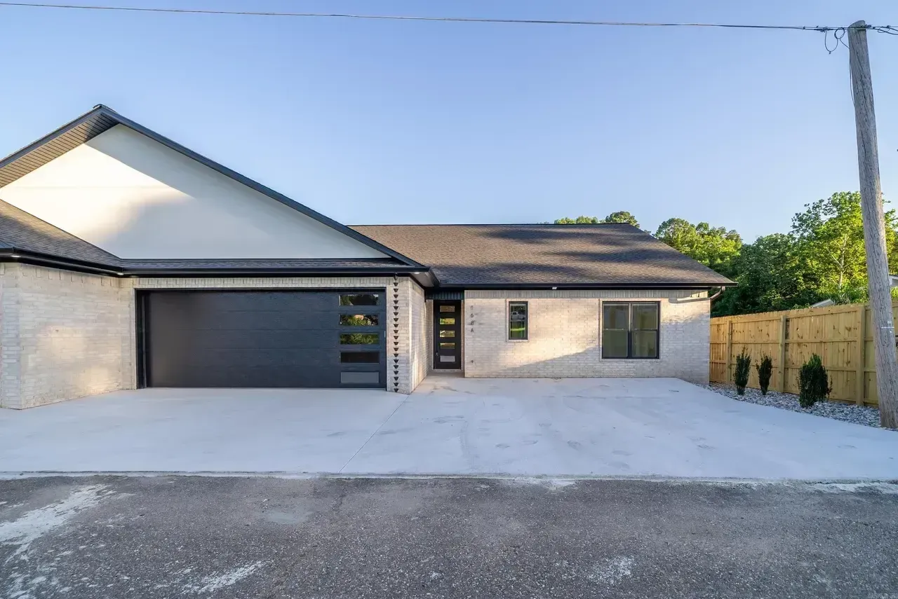 Modern single-story house with a large driveway, gray garage door, and beige exterior at dusk