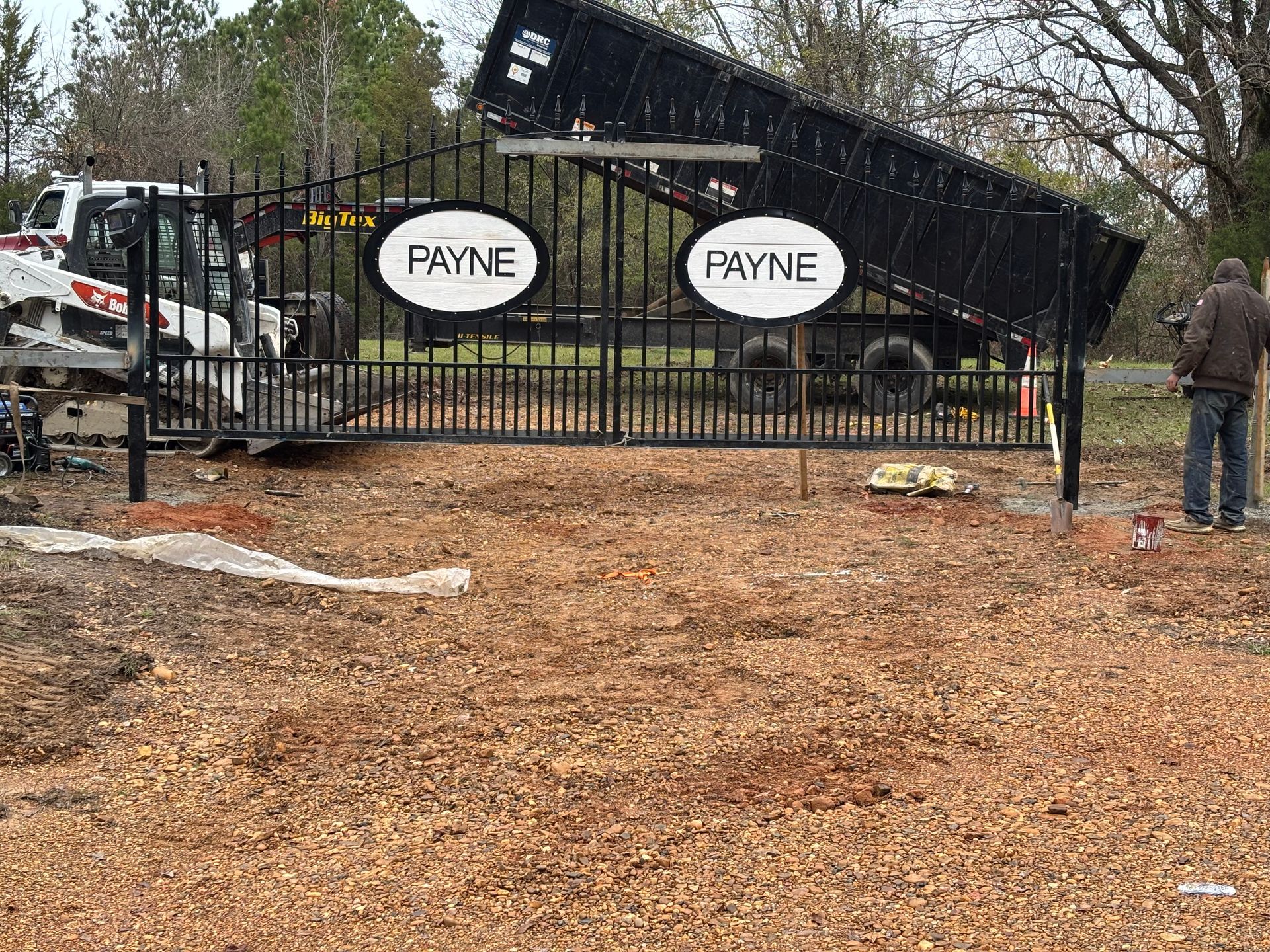 Black truck on a trailer behind a gate with two Payne signs in a wooded lot