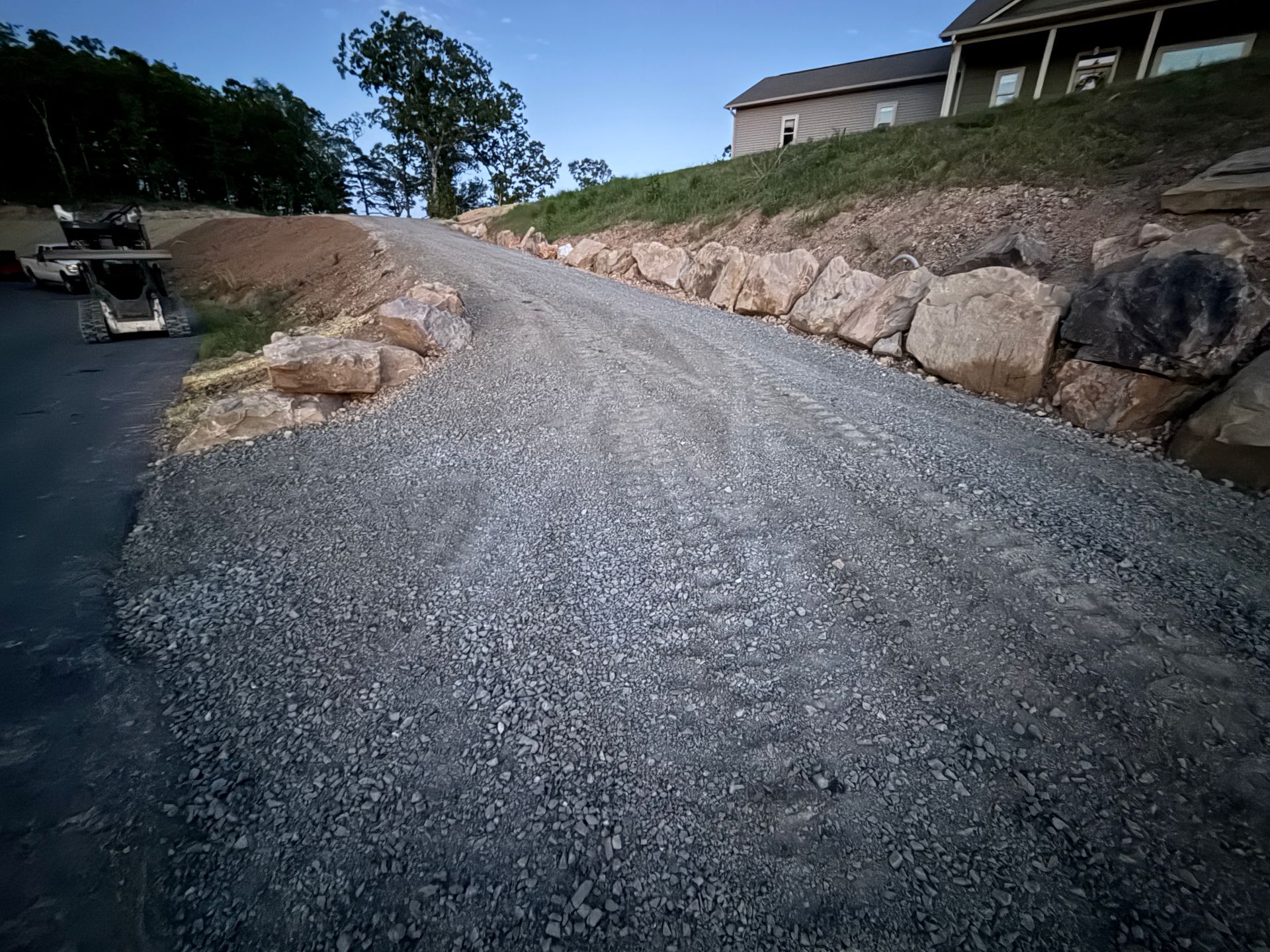 Gravel driveway curving uphill beside a stone retaining wall and house under a blue sky