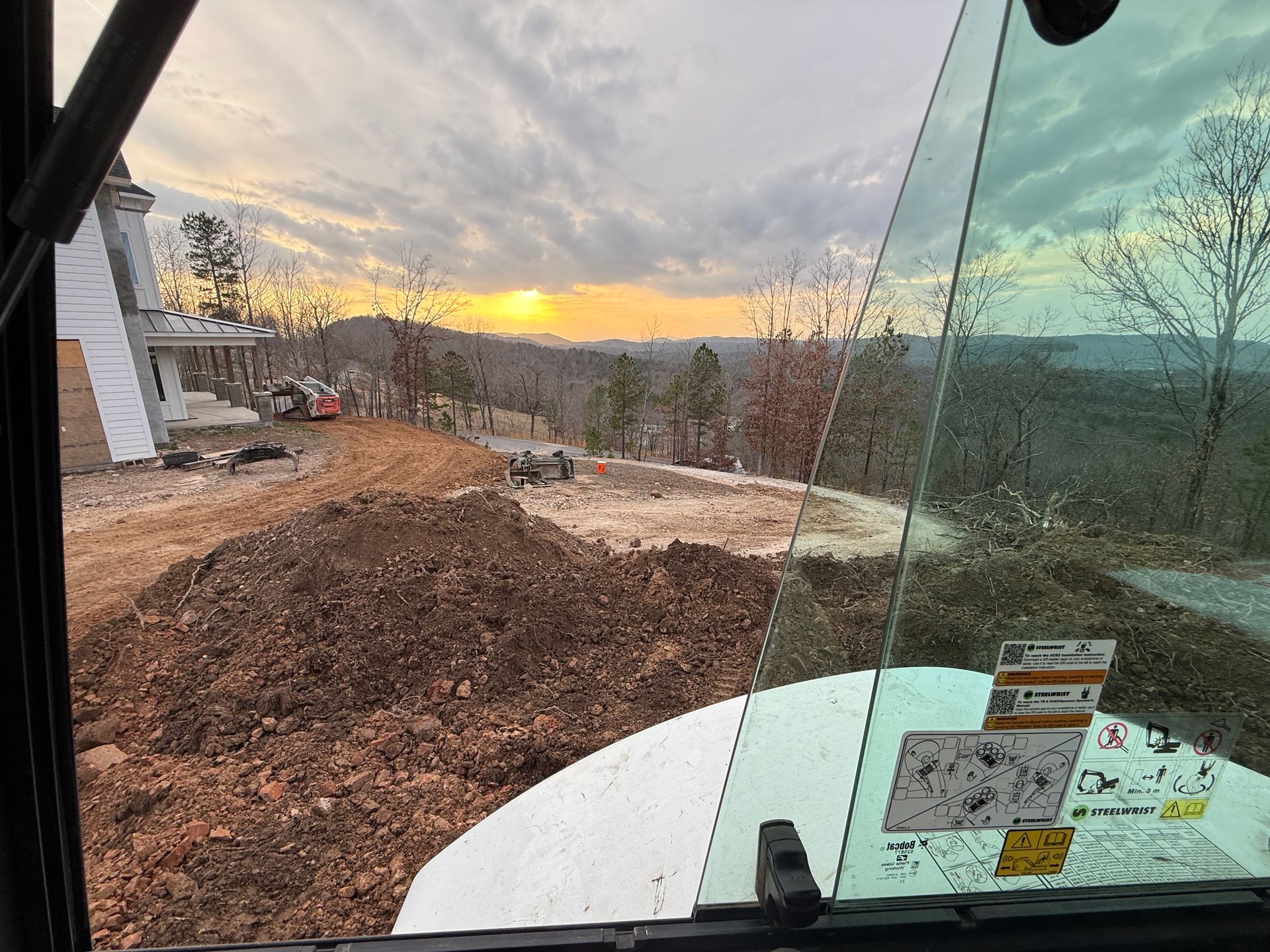 Dirt lot and rocks beside a glass building at sunset, with mountains in the distance