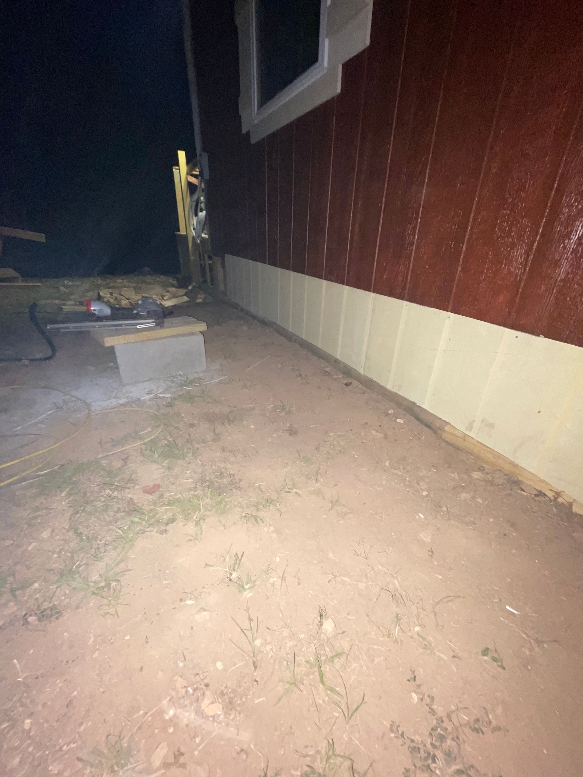 Dimly lit dirt path beside a red building with a window and a small concrete block.