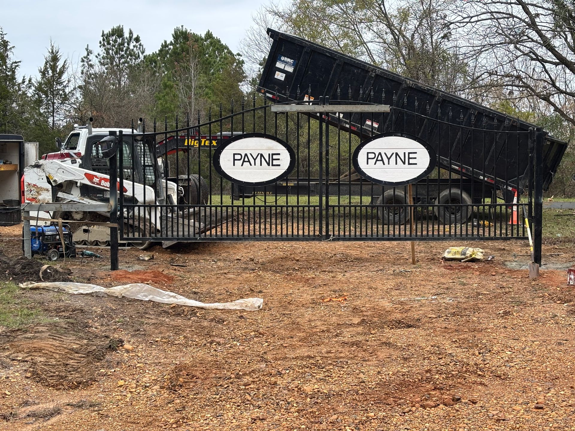 Flood damage outside Payne Automotive, with a black fence, mud, and debris under overcast skies