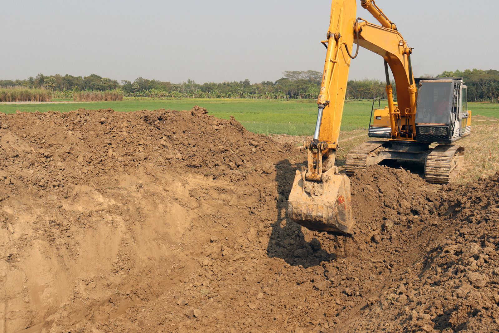Small excavator clearing a rocky dirt slope in a forested mountain area