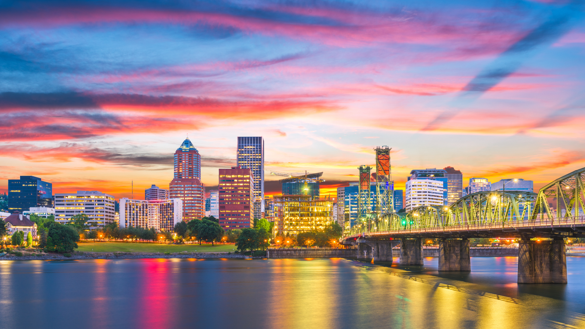 Portland, Oregon skyline at sunset, reflecting in the river with a bridge and colorful sky.