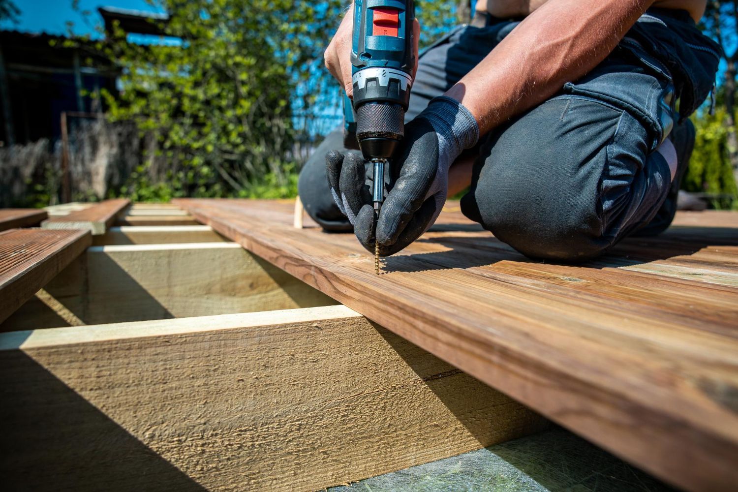 Person using a power drill to fasten wooden deck boards outdoors.