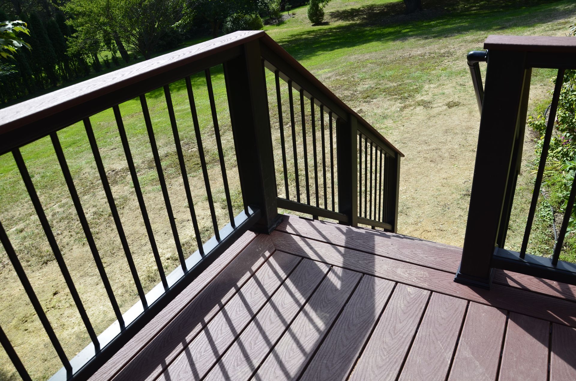 Wooden deck stairs with black railings leading to a grassy yard in sunlight