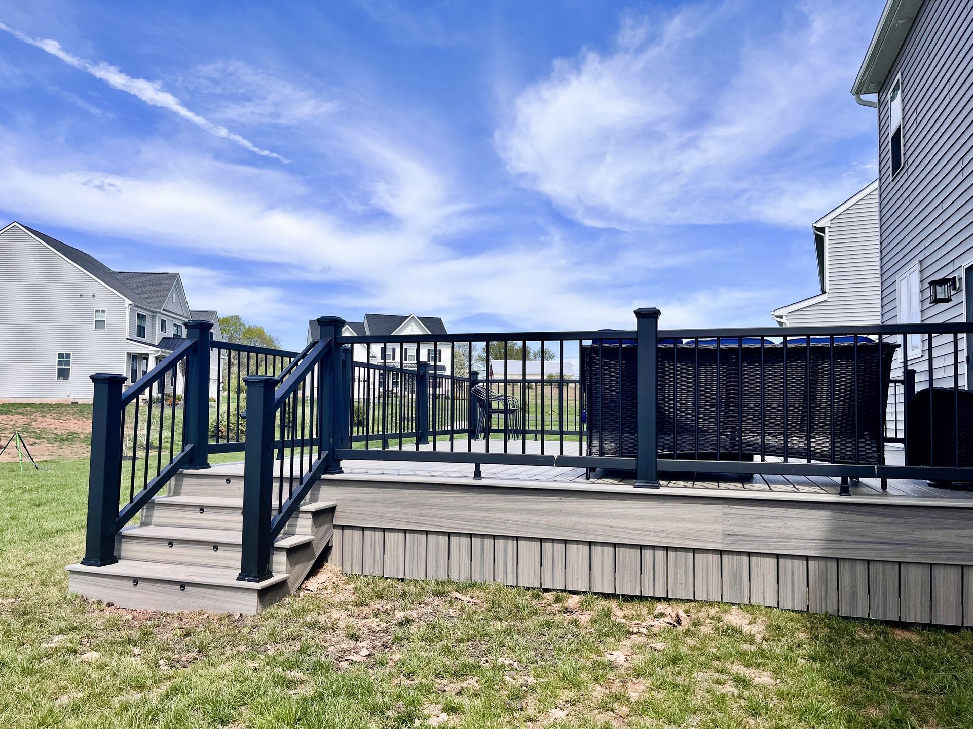 Backyard wooden deck with black railing and stairs under a blue sky, between neighboring houses
