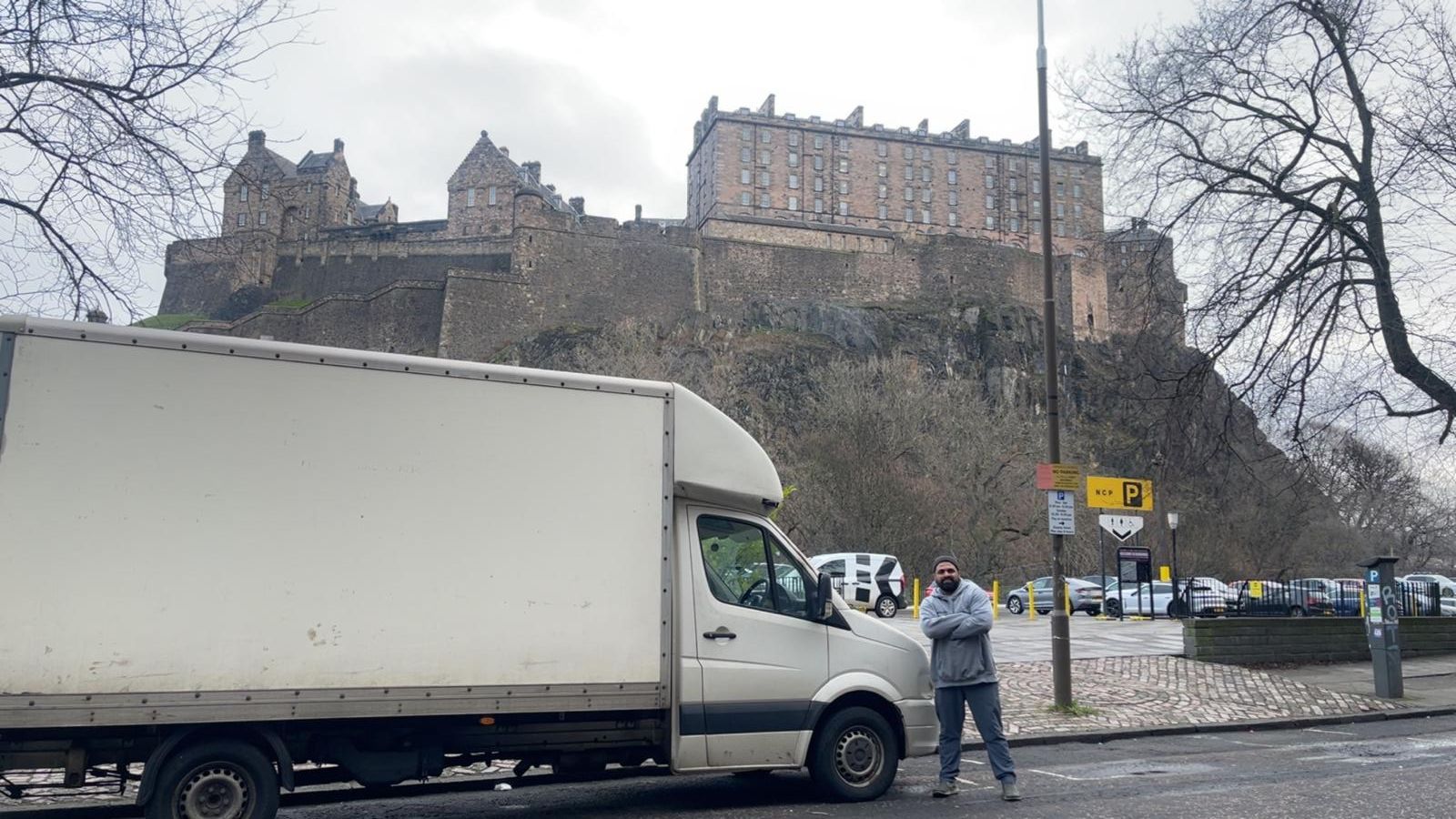 White box truck in foreground with a person beside it, castle on a hill in snowy winter background